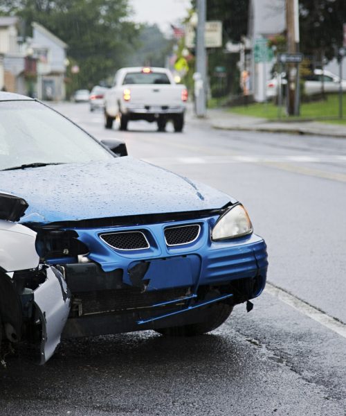 A damaged car after an accident on a wet urban road.