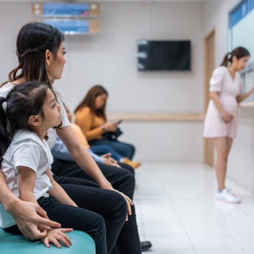 Asian family patient wait on line queue to receive medicine in hospital. Attractive mother and daughter sit on chairs, waiting the pharmacy counter to provides services to patients in medical center.