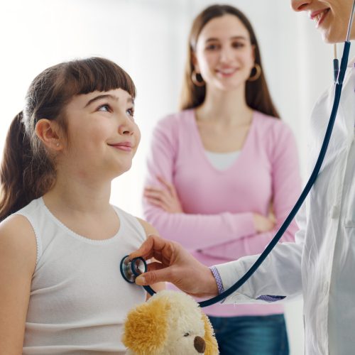 Female doctor examining a cute smiling girl with a stethoscope, the mother is next to her, children and healthcare concept